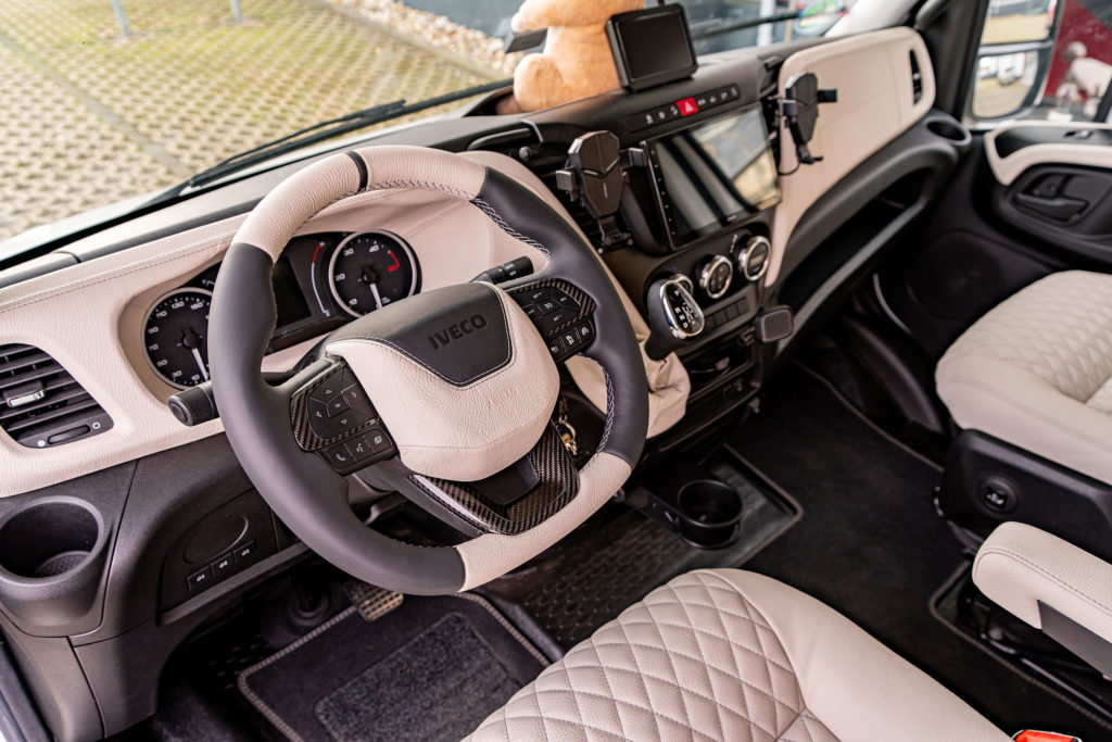 Weitwinkelansicht des Fahrerbereichs eines Wohnmobils mit Lenkrad, Instrumententafel und Mittelkonsole, alles in einer beige-schwarzen Farbgebung.